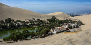 Huacachina Oasis surrounded by sand with mountains in background.