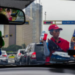 Woman standing in Lima traffic, dressed in red, selling bottled drinks.